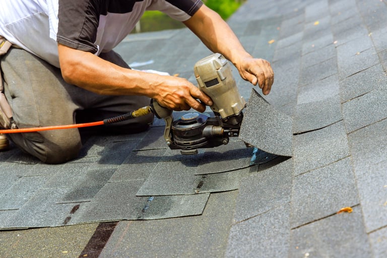 Construction roofer using pneumatic air nail gun installing new bitumen shingles on residential roof