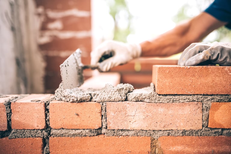 Bricklayer worker installing brick masonry on exterior wall with trowel